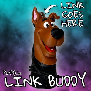 Puede incluir: Un Puffco Link Buddy con forma de Scooby-Doo marrón con una base negra y un cordón negro. El texto "LINK GOES HERE" y "LINK BUDDY" se muestran en blanco. El fondo es un degradado de verde azulado, morado y negro.