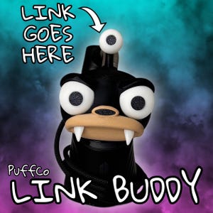 May include: Black "Link Buddy" accessory with cartoon features: large white eyes with black pupils, a tan mouth with two fangs, and a white eyeball on top. Text reads "LINK GOES HERE" and "Puffco LINK BUDDY".