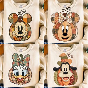 Puede incluir: Cuatro sudaderas color crema con personajes de Disney diseñados como calabazas. Mickey Mouse, Minnie Mouse, Daisy Duck y Goofy están representados con cuerpos de calabaza de patchwork y detalles decorativos, perfectos para otoño y Halloween.