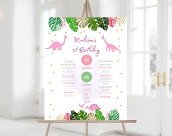 Puede incluir: Un póster de primer cumpleaños rosa y verde con temática de dinosaurios. El póster incluye el nombre del niño, la edad, el peso, la altura y otros datos divertidos. Presenta un dinosaurio rosa con una corona y un dinosaurio verde con un diente.