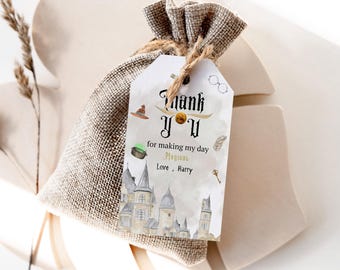 Può includere: Un'etichetta di ringraziamento bianca con un design oro e nero. L'etichetta presenta un castello, un calderone, un cappello, una piuma, una chiave e degli occhiali. Il testo sull'etichetta dice "Grazie per aver reso la mia giornata Magica Amore, Harry".