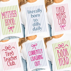 May include: White t-shirts with various phrases in colorful text, including "Motherhood," "Literally born to dilly daily," and "Tired Moms Club." Each design features a bow graphic and vertical striped background.