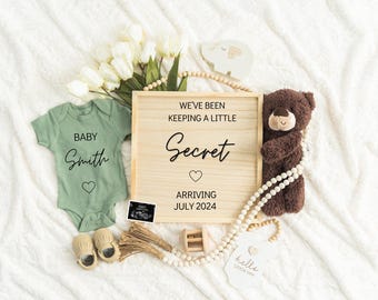 May include: A wooden sign with the text "We've been keeping a little secret. Arriving July 2024."  A green baby onesie with the text "Baby Smith" and a heart. A brown teddy bear and a white beaded garland.