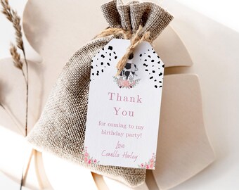 Könnte beinhalten: Ein kleiner Geschenkbeutel aus Jute mit einem Anhänger mit der Aufschrift "Danke" für eine Geburtstagsfeier. Der Anhänger hat eine Kuh-Illustration und florale Akzente. Der Anhänger ist mit Bindfaden an der Tasche befestigt.