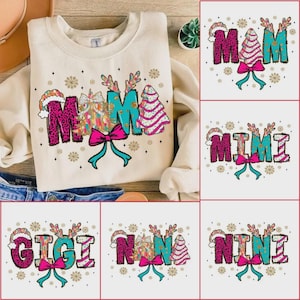 Puede incluir: Una sudadera color crema con la palabra "MAMA" en un diseño festivo. Las letras están decoradas con estampado de leopardo, turquesa y un motivo de árbol de Navidad. Un lazo rosa y copos de nieve completan el tema navideño. Diseños adicionales incluyen "MIMI", "GIGI", "NANA" y "NINI".