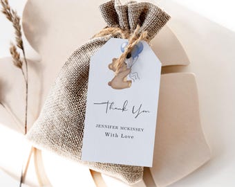 May include: A white thank you tag featuring a brown bear holding blue balloons. The tag is attached to a small hessian bag. The text on the tag reads "Thank You" with the name "Jennifer Mckinsey" and the phrase "With Love" underneath.