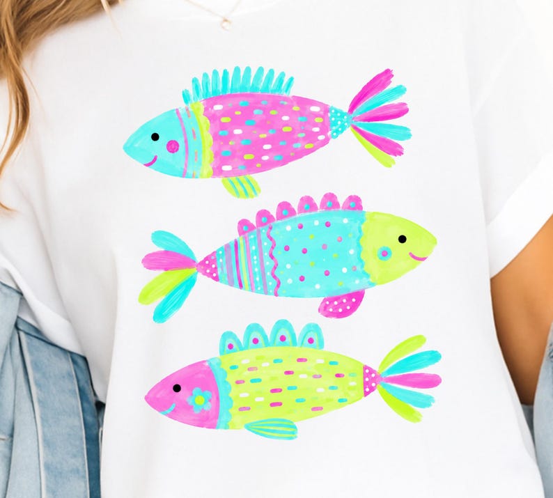 Op de afbeelding: Wit T-shirt met drie kleurrijke visillustraties. Elke vis heeft een uniek ontwerp met roze, blauwe en gele accenten. De vissen hebben lachende gezichten en zijn verticaal op het shirt geplaatst.