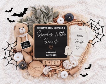 Op de afbeelding: Een baby-aankondiging met Halloween-thema met een krijtbord waarop staat "We have been keeping a spooky little secret. Arriving July 2025. Baby." Het bord is omringd door een teddybeer, een baby-romper, een spinnenweb en andere Halloween-decoraties.