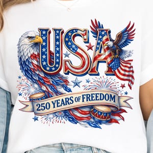 May include: White t-shirt featuring a patriotic design with the word "USA" in red, white, and blue, along with an eagle, stars, and fireworks. The text "250 YEARS OF FREEDOM" is displayed on a banner.
