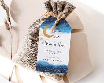 May include: A blue and gold thank you tag with a crescent moon and stars. The text reads "We are over the moon! Thank you for showering us with love! Carman Jones Baby Shower".