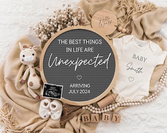 May include: A gray letter board with the text "The best things in life are unexpected" and "Arriving July 2024". A white onesie with the text "Baby Smith" and a small heart. A stuffed giraffe, a baby onesie, and a wooden block that says "Baby".