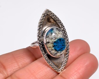 May include: A silver ring featuring a large, oval-shaped stone with a blue, white, and gray pattern. The ring has a decorative, elongated setting with a textured border, showcasing a unique gemstone design.