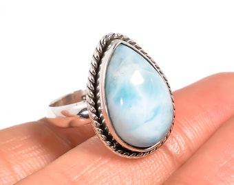 May include: A sterling silver ring featuring a pear-shaped, light blue larimar gemstone. The stone is set in a decorative, twisted rope-like bezel. The ring is shown on a hand.