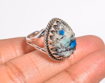 May include: A silver ring featuring a large, teardrop-shaped stone. The stone has a white base with blue and gray patterns. The ring's setting has a decorative rope-like border and a split band.