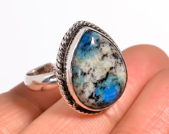 May include: A silver ring featuring a large, teardrop-shaped k2 stone. The stone displays a mix of blue, white, and black patterns. The ring has a twisted rope design around the stone and a simple band.