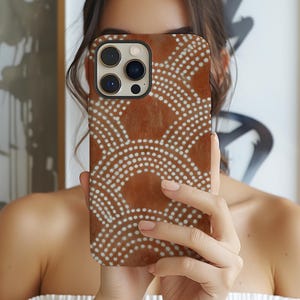 May include: A brown phone case with a white dotted pattern. The case has a textured appearance and a black border around the camera lenses. The design features semi-circular patterns of white dots against a brown background.