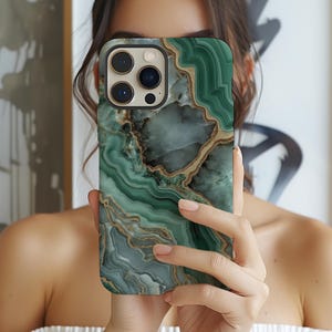May include: A smartphone case with a green and gold marble design. The case has a glossy finish and features a swirling pattern of green, gold, and white colors. The case has a camera cutout and button cutouts.