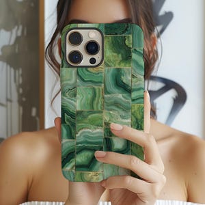 May include: Green and gold iPhone case with a malachite design. The case features a mosaic pattern of rectangular tiles in varying shades of green, with gold accents. The phone's camera lenses are visible.