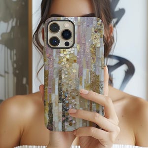 May include: A mosaic-style phone case in gold, pink, and beige. The rectangular case has a textured surface. The phone case is held in front of a person's face. The case is designed for a smartphone.
