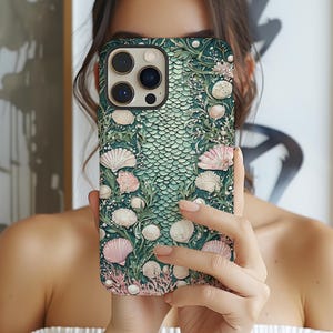 May include: A green and pink seashell-themed phone case. The case features a scale-like pattern in the center, surrounded by detailed illustrations of seashells, coral, and seaweed. The case has a raised, textured design and a glossy finish.