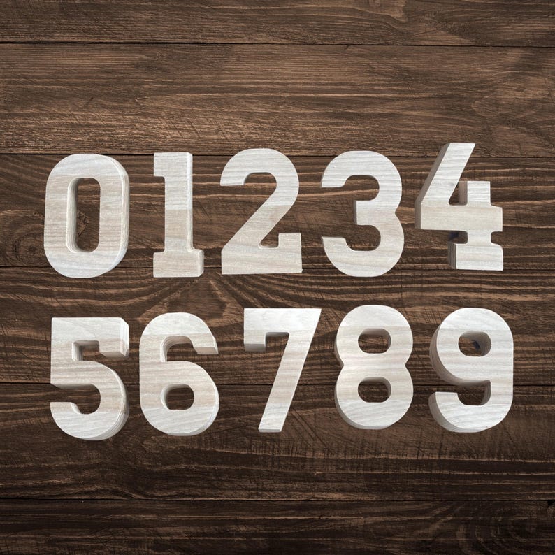 May include: A set of ten individual wooden numbers ranging from zero to nine. Each number is crafted from light-colored wood with a visible natural grain pattern. The digits are arranged in two horizontal rows, with zero through four on top and five through nine on the bottom, displaying a clean, block-style font design.