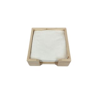 May include: A wooden napkin holder with a white napkin inside. The holder is made of natural wood and has a simple design.