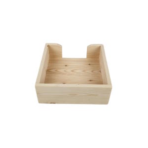 May include: A natural wood square tissue box holder with a simple design. The holder is made of unfinished wood and has a rectangular opening for tissues.
