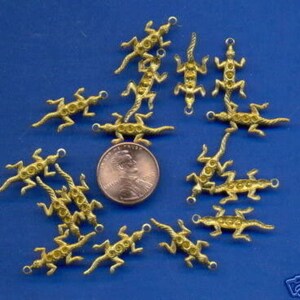 May include: A collection of 12 gold-toned lizard charms with rhinestones. The charms are arranged in a circle on a blue background.