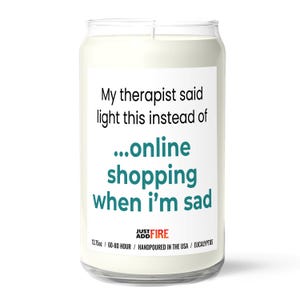 May include: A clear glass jar candle with a white label. The label reads "My therapist said light this instead of...online shopping when I'm sad." The candle is 13.75oz and hand-poured in the USA.