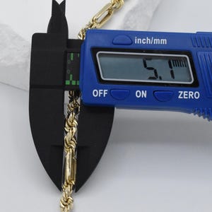 May include: A gold-colored rope chain is measured with a blue digital caliper. The caliper displays a measurement of 5.1 inches. The chain is placed between the caliper's jaws for an accurate reading. The caliper has an "OFF", "ON", and "ZERO" button.