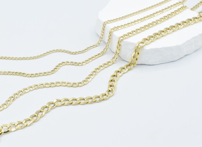 May include: Four gold chains of different thicknesses, laid out on a white surface.