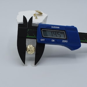 K&ouml;nnte beinhalten: Goldfarbene Ohrstecker mit strukturierter Oberfl&auml;che werden mit einem blauen digitalen Messschieber gemessen. Der Messschieber zeigt ein Ma&szlig; von 1,45 cm an. Zus&auml;tzliche Ohrringe befinden sich auf einer wei&szlig;en Oberfl&auml;che.