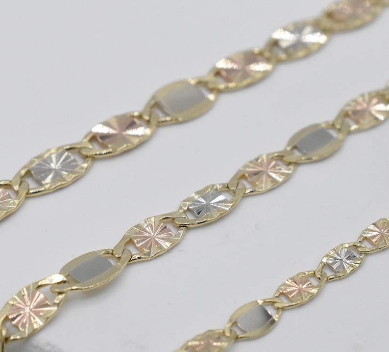 Puede incluir: Primer plano de tres cadenas de oro con una mezcla de eslabones de oro amarillo, blanco y rosa. Las cadenas presentan un patr&oacute;n repetitivo de eslabones ovalados y en forma de estrella, creando un dise&ntilde;o texturizado. Fondo blanco.