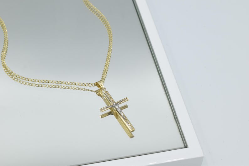Puede incluir: Un collar de cadena de oro con un colgante de cruz de dos tonos. La cruz est&aacute; hecha de oro y plata y presenta una peque&ntilde;a figura de Jes&uacute;s.