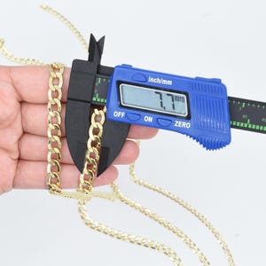 May include: A gold chain necklace is being measured with a blue digital caliper. The caliper reads 7.7 mm.