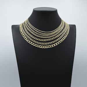 Puede incluir: Un conjunto de collares de cadena curb de oro de diferentes anchos, exhibidos en un soporte de terciopelo negro. Las cadenas están ordenadas por tamaño, con la cadena más pequeña en la parte superior y la cadena más grande en la parte inferior.