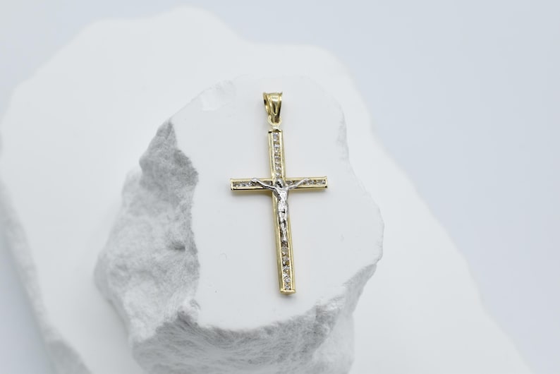 Puede incluir: Un colgante de cruz de oro y plata con una peque&ntilde;a figura de Jesucristo en la parte delantera. La cruz est&aacute; engastada con peque&ntilde;as piedras transparentes.