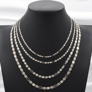 Puede incluir: Conjunto de collares plateados expuestos sobre un maniqu&iacute; negro. Los collares, de diferentes longitudes, presentan cada uno una delicada cadena con eslabones ovalados. Las cadenas est&aacute;n dispuestas en capas, creando un efecto en cascada.