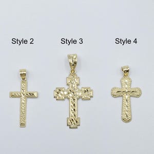 Puede incluir: Cinco colgantes de cruz dorados, cada uno con un diseño único. Los estilos varían de simples a ornamentados, con superficies texturizadas y detalladas. Los colgantes se muestran sobre un fondo blanco liso.