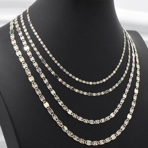 Puede incluir: Exhibici&oacute;n de cinco collares plateados de diferentes estilos y longitudes. Las cadenas presentan eslabones ovalados y geom&eacute;tricos. Los collares est&aacute;n colocados sobre un maniqu&iacute; negro, resaltando sus dise&ntilde;os.