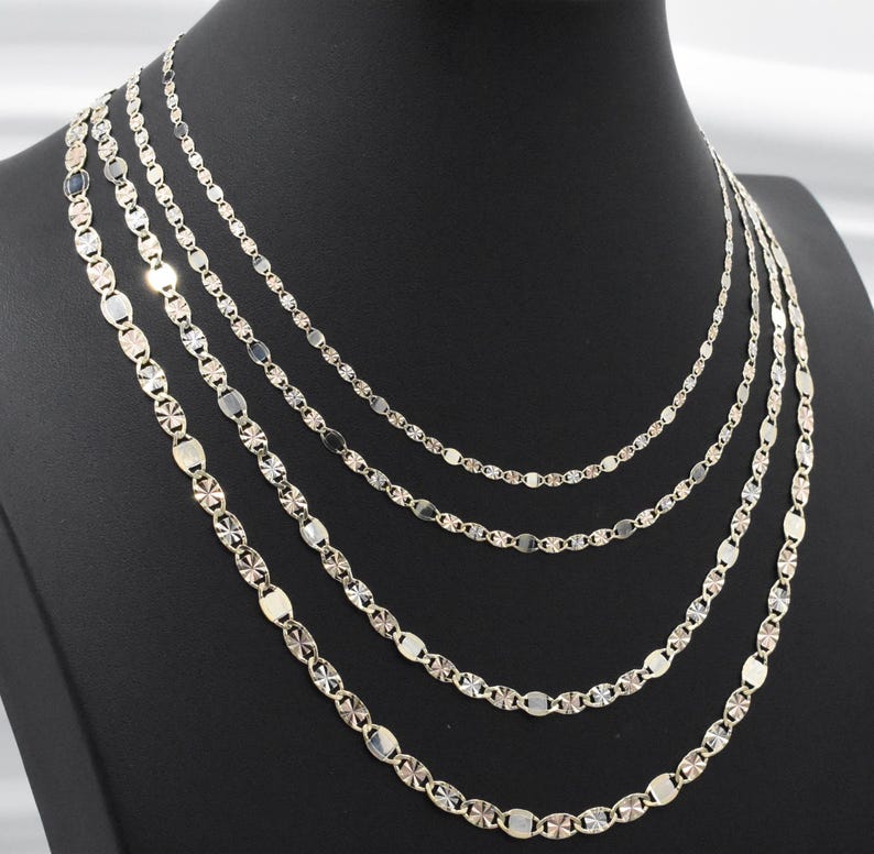 Puede incluir: Exhibici&oacute;n de cinco collares plateados de diferentes estilos y longitudes. Las cadenas presentan eslabones ovalados y geom&eacute;tricos. Los collares est&aacute;n colocados sobre un maniqu&iacute; negro, resaltando sus dise&ntilde;os.