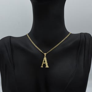 Puede incluir: Un collar de cadena de oro con un colgante de letra A de oro texturizado.