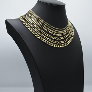 May include: A set of gold curb chains of varying widths displayed on a black mannequin bust. The chains are arranged in order of size, with the smallest chain at the top and the largest chain at the bottom.