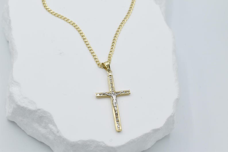 Puede incluir: Un collar de cadena de oro con un colgante de cruz de dos tonos. La cruz est&aacute; hecha de oro y plata y presenta un dise&ntilde;o detallado de una figura en la cruz.