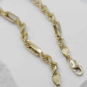 May include: A gold-colored chain necklace with a rope-like design and rectangular links. The necklace has a lobster clasp closure. The metal is stamped with "10K FMG".