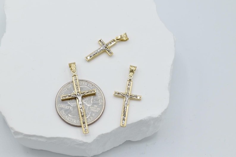 Puede incluir: Tres colgantes de cruz de oro y plata de diferentes tama&ntilde;os. La cruz m&aacute;s grande est&aacute; al lado de una moneda de un cuarto de d&oacute;lar estadounidense para comparar el tama&ntilde;o.