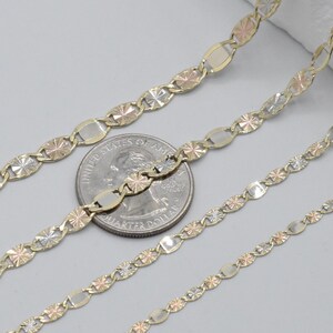 Puede incluir: Primer plano de tres cadenas de oro con una moneda de veinticinco centavos para comparar el tama&ntilde;o. Las cadenas presentan una mezcla de oro amarillo, rosa y blanco. Las cadenas tienen un patr&oacute;n repetitivo de eslabones ovalados y en forma de estrella.