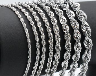 Puede incluir: Una colección de cadenas de cuerda plateadas de diferentes grosores. Las cadenas se muestran sobre una superficie negra, mostrando su diseño de cuerda trenzada. La imagen destaca los diferentes tamaños y la calidad reflectante del metal.