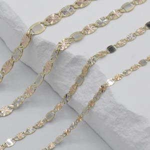 Puede incluir: Cuatro cadenas de oro con eslabones ovalados y en forma de estrella alternados. Las cadenas presentan una mezcla de oro amarillo, blanco y rosa, creando un efecto tricolor. Las cadenas se muestran sobre una superficie blanca texturizada.