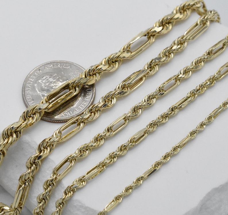 May include: Close-up of several gold-colored chain necklaces in varying styles and sizes. The chains are displayed on a white surface, with a U.S. quarter coin for size comparison. The chains have different link designs, including rope and elongated oval links.